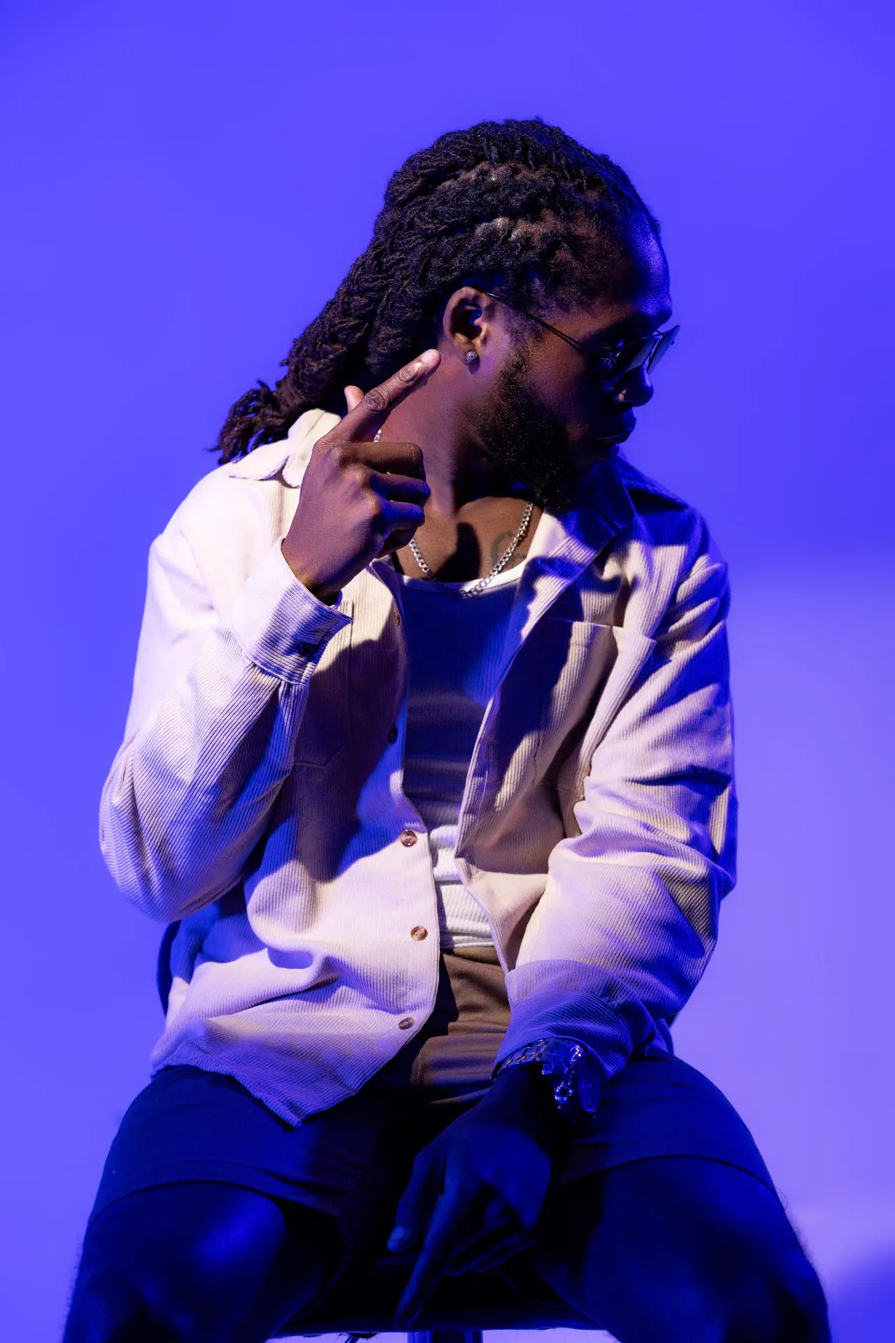 Saint Chris seated under blue studio light with his head lowered.